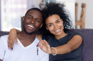 African couple sitting on couch holding keys from new house