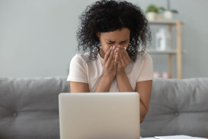 African American woman blowing nose, holding handkerchief, sneezing at home