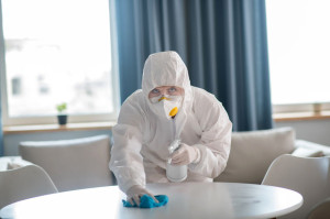 Woman in white workwear and protective gloves cleaning the table surface