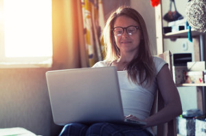 pretty woman with laptop sitting in chair in morning sunlight and typing