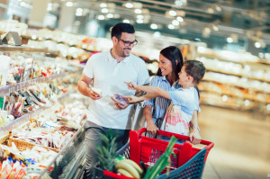 Happy family with child and shopping cart buying food at grocery