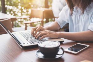 Young woman using smart phone and laptop with cup of coffee in cafe