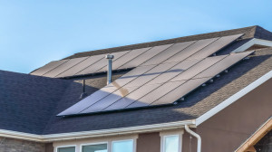 Panorama Gray roof of home with solar panels and pipe vents against blue sky background