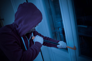 Hooded burglar forcing window to rob in the house at night