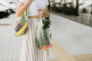 Zero waste concept with copy space. Woman holding cotton shopper and reusable mesh shopping bags with vegetables, products. Eco friendly mesh shopper. Zero waste, plastic free concept.