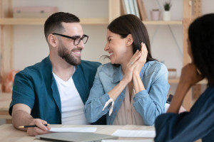 Excited young couple sign deal at office meeting