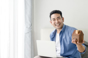 Asian man holding house in his hand and using laptop, real estat