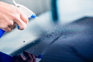 Hand spraying cleaning substance on the surface of a blue car