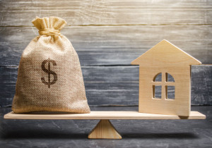 A money bag and a wooden house on the scales. The concept of real estate purchase. Sale of property. Payment of the mortgage. Redemption of taxes. Tax refund. Legacy / Inheritance tax concept