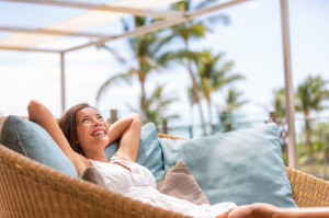 Luxury hotel home living woman relax enjoying sofa furniture of outdoor patio. Beautiful young multiracial Asian girl relaxing day dreaming for rich early retirement in getaway tropical house.