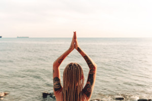 Young girl with tattoo practices yoga at sea. Gestures of meditation.