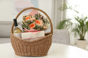 Wicker basket with gifts on table indoors. Space for text
