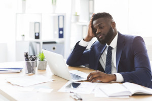 Exhausted young businessman working with laptop in office