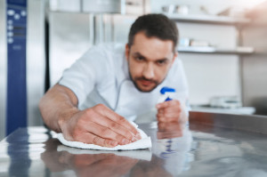 Hygienic precautions. Worker in restaurant kitchen cleaning down after service. Selective focus on his hand