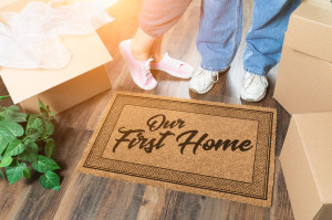 Man and Woman Unpacking Near Our First Home Welcome Mat, Moving Boxes and Plant.