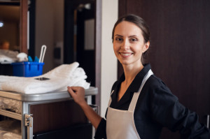 A portrait of a smiling housekeeping lady with a cart