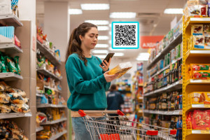 A young Caucasian woman scans the qr code on a food package using her smartphone. Qr code icon above the product. In the background is a supermarket. Concept of modern technologies and shopping