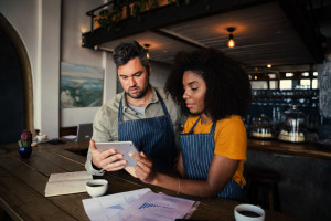 Concerned male and female coffee shop owners scrolling on tablet in rustic coffee shop.