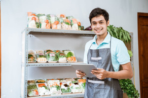 Man selling vegetables smiling while using a digital tablet