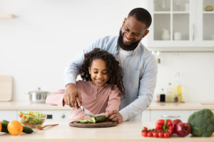 African american father teaching daughter how to prepare salad