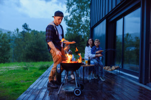 Happy father preparing a barbecue on a family vacation on the terrace of their modern house in the evening.