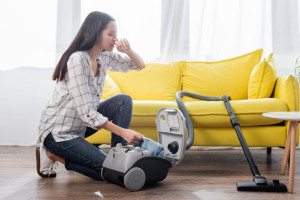 young woman suffering from allergy while holding dust bag near vacuum cleaner