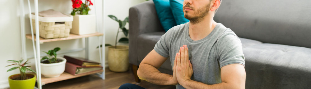 Adult man sitting in a yoga mat and meditating at home