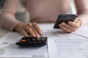 Close up young woman calculating domestic utility bills, using smartphone.