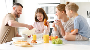 Young happy family with two cute little kids having breakfast together in kitchen and smiling