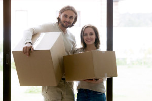 Couple standing with unopened cardboard boxes looking at camera