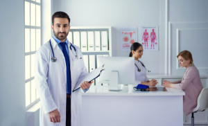 Smiling doctor man standing in front of his team and patient