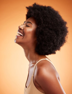 Cosmetics, black woman and smile with natural beauty with brown studio background being confident, happy and with afro. Makeup, female and African American girl being proud, laugh and clear skincare.