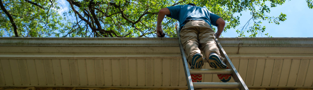 Low angle view of off center man on ladder cleaning gutters of a stone home