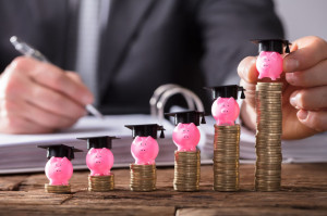 Businessperson Placing Piggybank With Graduation Cap