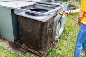 Person cleaning dirty condenser coils on an air conditioner syst