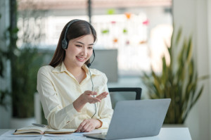 Portrait of happy smiling female customer support phone operator at workplace. Asian