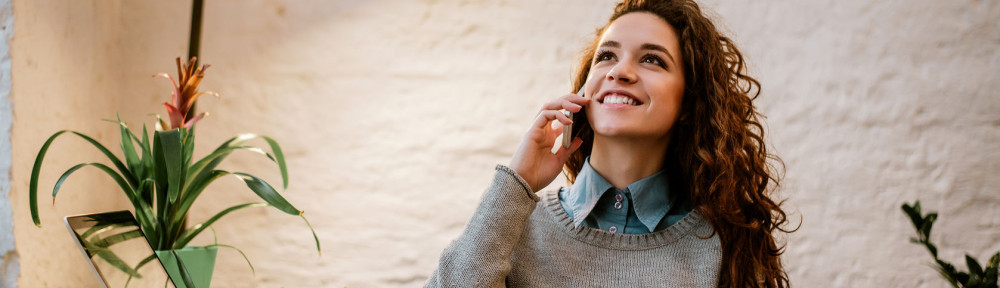 Cheerful woman talking on phone at desk in modern office.