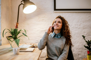 Cheerful woman talking on phone at desk in modern office.