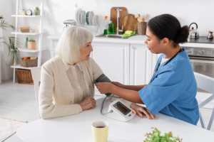 multiracial nurse measuring blood pressure of senior woman with grey hair