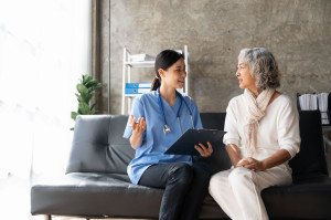 Happy patient is holding caregiver for a hand while spending time together. Elderly woman in nursing home and nurse.