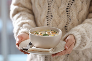 Young woman with bowl of cream soup on blurred background, close