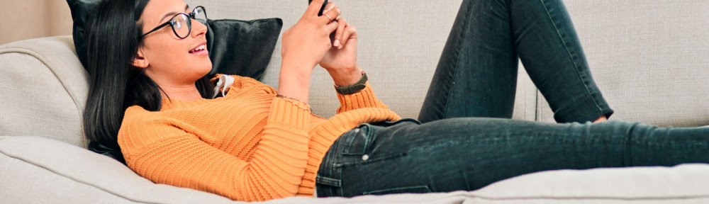 Sharing me time with social media. a young woman using a smartphone and relaxing on the sofa at home.