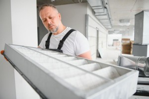 A male worker holds an air filter for air conditioning in an office space. Installation of an air conditioner.