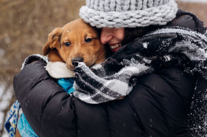 stylish hipster woman hugging and smiling cute puppy in snowy co