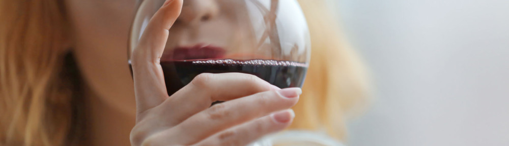 Young woman with glass of red wine on light blurred background