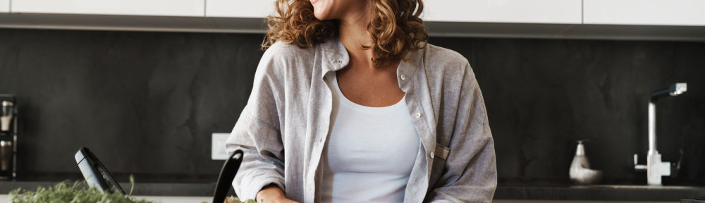 Happy young woman making a salad at the kitchen