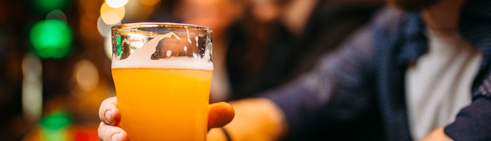 Male person holds glass with beer at bar counter