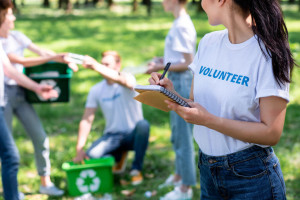 woman writing in textbook while volunteers cleaning park