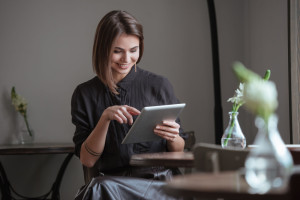 Cute lady sitting near window in cafe while using tablet