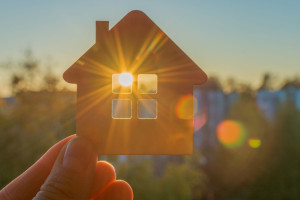 in hand a close-up of a small sketchy wooden house, through the window of which the sun's rays of the setting or rising sun are visible. The idea is to find your own home, hoping for a new day.